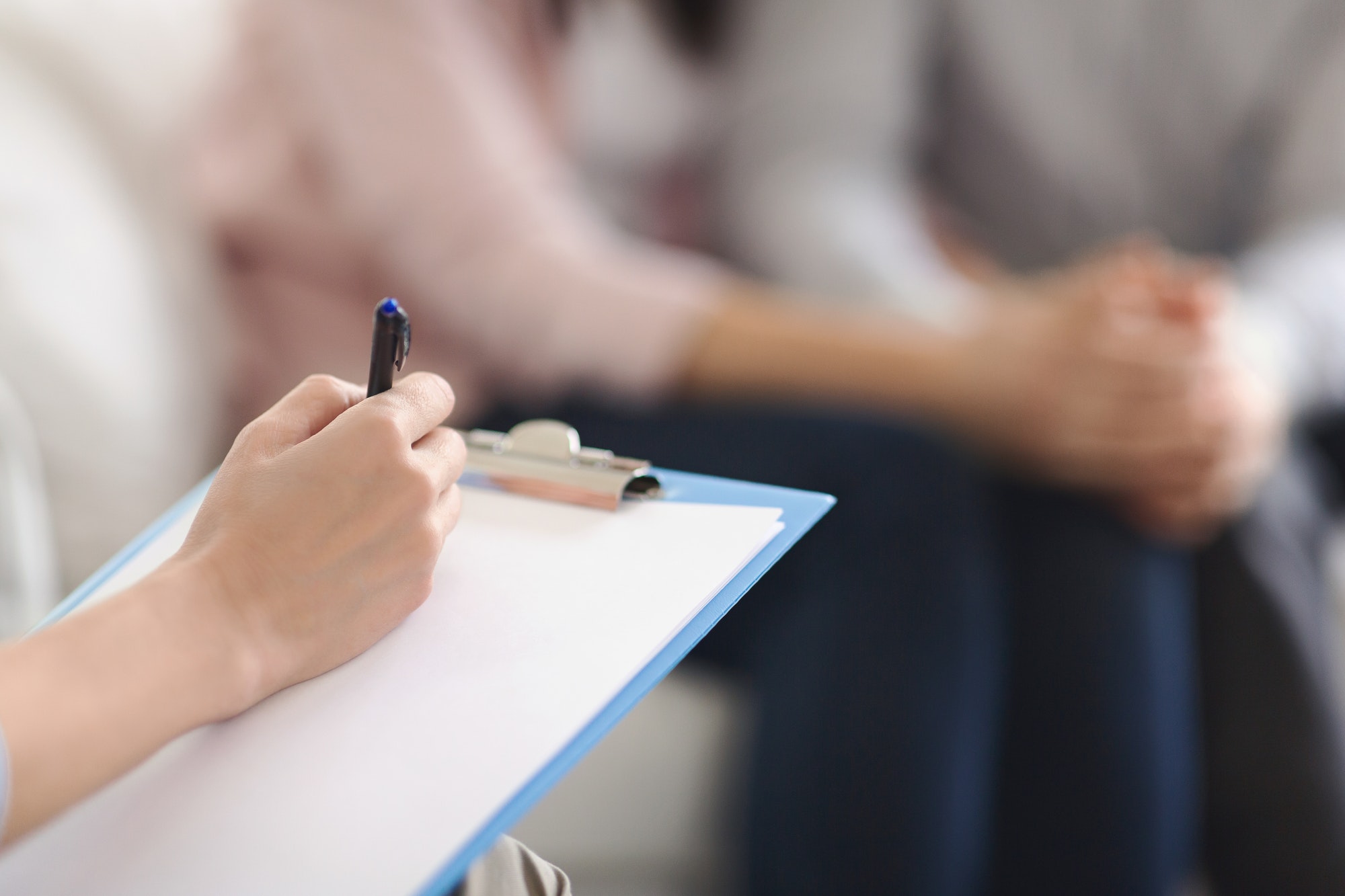 Psychologist writing in blank notepad at family counseling session Psychologist writing in blank notepad at family counseling session